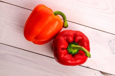 Two whole organic fresh juicy tasty bell peppers, close-up, on a painted white tabletop made of wood, top view.