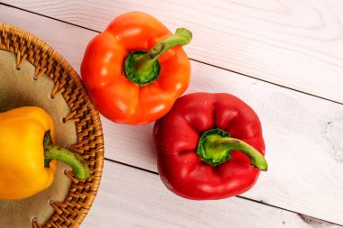 Three whole organic fresh juicy tasty bell peppers, close-up, on a ceramic plate, standing on a painted white tabletop made of wood, top view.