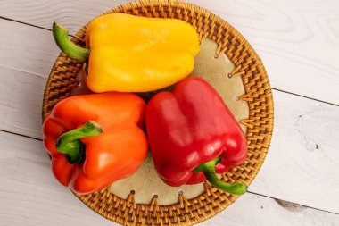 Three whole organic fresh juicy tasty bell peppers, close-up, on a ceramic plate, standing on a painted white tabletop made of wood, top view.