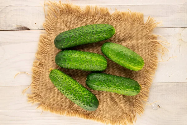 Several ripe green cucumbers with a jute napkin on a wooden table, close-up, top view.