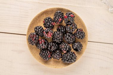 Several sweet blackberries with a ceramic saucer on a wooden table, close-up, top view.