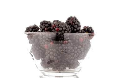 Several sweet blackberries in a glass bowl, close-up, isolated on a white background.