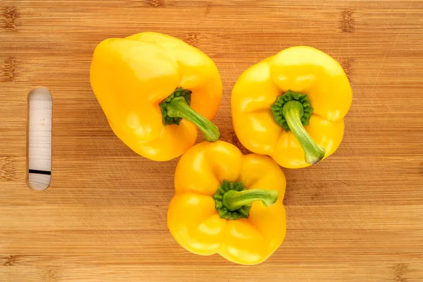 Three ripe yellow sweet peppers on a bamboo cutting board, close-up, top view.