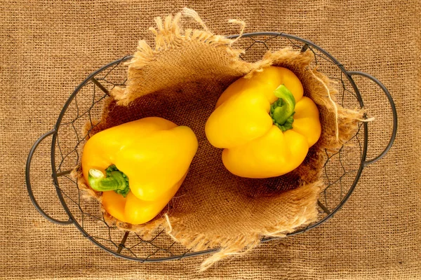 Two ripe yellow sweet peppers in a basket on jute fabric, close-up, top view.
