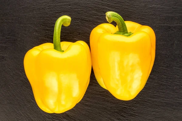 Two ripe yellow sweet peppers on a shale stone, close-up, top view.