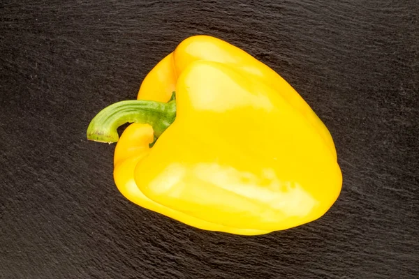 One ripe yellow sweet pepper on a slate stone, close up, top view.