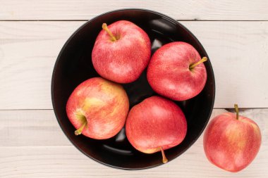 Tahta bir masanın üzerinde seramik siyah plakalı birkaç tatlı kırmızı elma, makro, üst manzara..