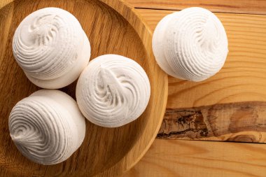 Yuvarlak bir bambu tepsisinin üzerinde birkaç tatlı marşmelov, ahşap bir masa, yakın çekim, üst manzara.