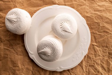 Beyaz seramik bir tabakta üç tatlı marşmelov, el işi kağıt üzerinde, yakın plan, üst manzara..