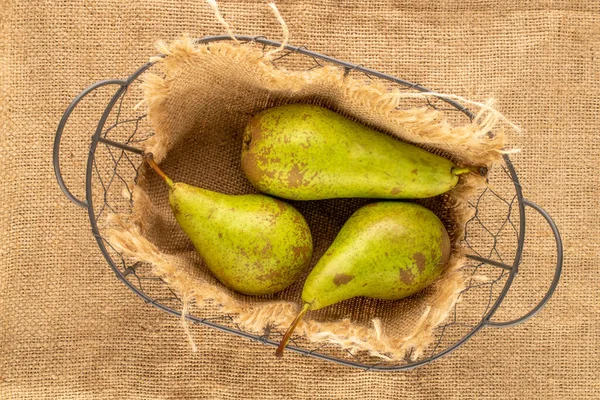Three juicy pears in a basket on a jute cloth, macro, top view.
