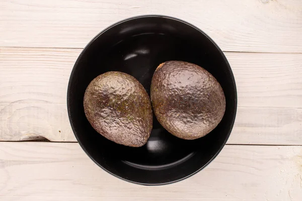 Due Avocado Maturi Con Piatto Ceramica Nera Tavolo Legno Macro — Foto Stock