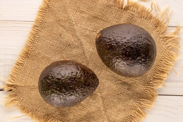 Two ripe avocados with a jute napkin on a wooden table, macro, top view.