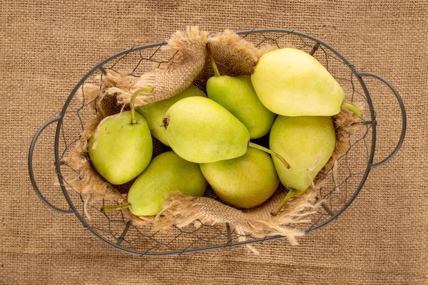 Several sweet pears in a basket on a jute cloth, macro, top view.
