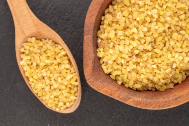 Tahta bardakta çiğ bulgur taneleri. Tahta taşın üstünde kaşık, makro, üst manzara..
