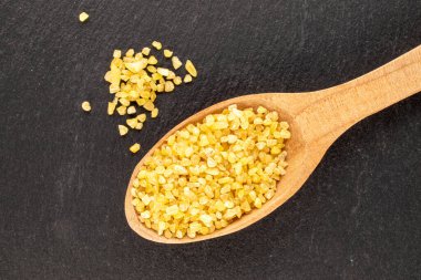 Tahta bir kaşıkta çiğ bulgur taneleri. Tahta taş, makro, üst manzara..
