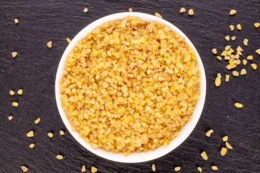 Tahta taş, makro, üst görünüm üzerinde beyaz bir çanakta çiğ bulgur taneleri.