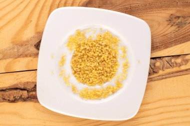 Tahta bir masada beyaz bir tabakta çiğ bulgur taneleri, makro, üst manzara..