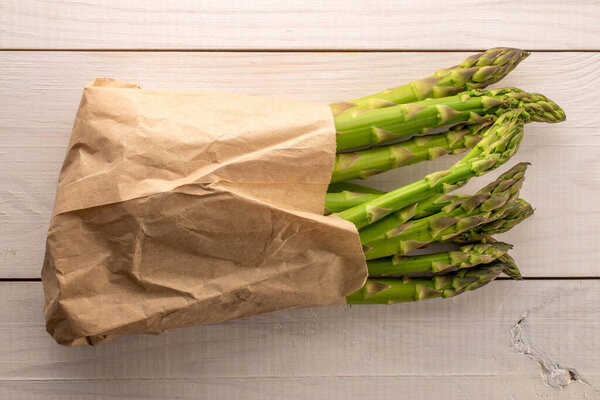 Несколько стеблей спелой органической спаржи в бумажном пакете на деревянном столе, крупным планом, вид сверху.