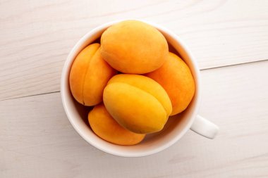 Beyaz seramik bir fincanda, beyaz ahşap bir masada, üst manzaralı, olgun, sarı ananas kayısıları..