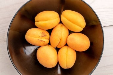 Siyah seramik tabakta birkaç tane olgun sarı ananas kayısı, yakın plan, beyaz ahşap masa, üst manzara..