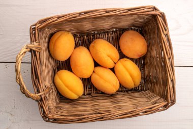 Metal sepetin içinde birkaç organik sarı ananas kayısı, yakın plan, beyaz ahşap masa, üst görüş..