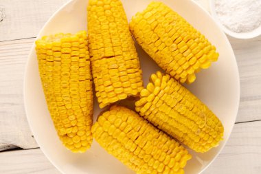 Tahta bir masa, makro, üst görünüm üzerinde beyaz bir plaka ile birkaç güzel kokulu haşlanmış mısır.