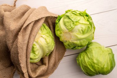  Üç parlak yeşil lahana kafasında jüt bir çanta, ahşap bir masa, üst görünüm.