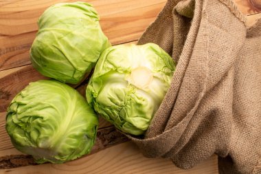  Üç parlak yeşil lahana kafasında jüt bir çanta, ahşap bir masa, üst görünüm.