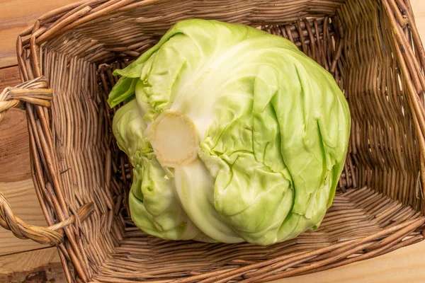 One ripe juicy heads of cabbage in a wicker basket of vines, on a wooden table, top view.