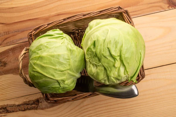 Two ripe juicy heads of cabbage in a wicker basket of vines, on a  wooden table, top view.