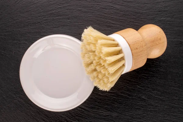 One dish brush with white ceramic saucer on slate stone, macro, top view.