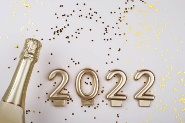 Şampanya şişesinin düz kompozisyonu ve bej arka plan fotokopi alanı üzerine konfeti, yeni yıl 2022