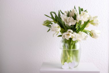 Bouquet of white tulips in a vase against white wall copy space 