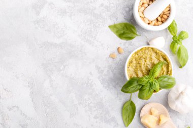 Pesto sauce and ingredients, black cheese board, basil, garlic, pine nuts, olive oil on grey stone background with copy space