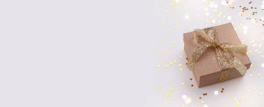 Gift box wrapped in craft paper with gold ribbon and stars on grey stone, banner