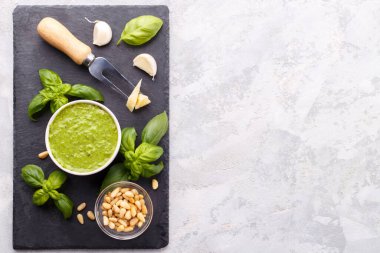 Pesto sauce and ingredients, cheese, basil, garlic, pine nuts, olive oil on black cheese board and grey stone background with copy space