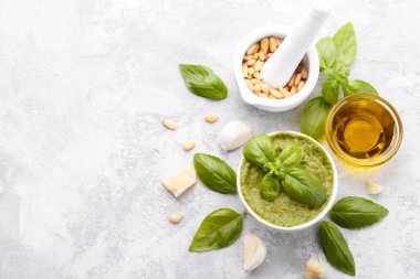 Pesto sauce and ingredients, cheese, basil, garlic, pine nuts, olive oil on grey stone background with copy space