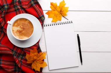 Cup of hot coffe latte and notepad, checkered table cloth on the white wooden table, autumn compositionwit copy space