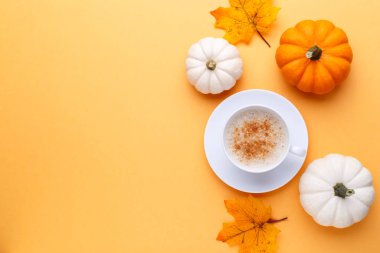Cup of coffee and white and orange pumpkins on the orange background, autumn flatlay concept
