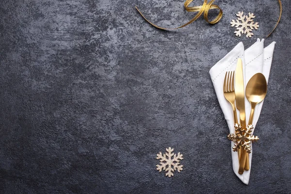 Table setting with golden cutlery and white napkin on the black stone table, Christmas or new year card or menu template copy space flat lay