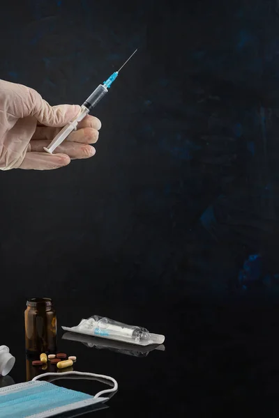 Coronavirüs ve diğer virüslere karşı aşı kavramı. İlaçlar, şırınga, tıbbi maske, karanlık arka planda hastalığa karşı eldivenler. Seçici odak.
