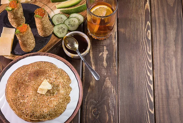 Siyah bir taş üzerinde kırmızı havyarlı gözleme, tereyağlı gözleme, salatalık, avokado, peynir, meyve çayı.