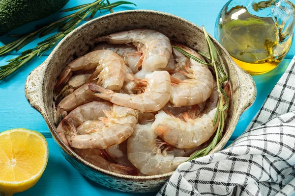 Beyaz karides, Pasifik beyaz karidesi ya da limon, biberiye, avokado, mavi ahşap arka planda zeytinyağı içeren yuvarlak bir kâsede kral karidesi. seçici odak