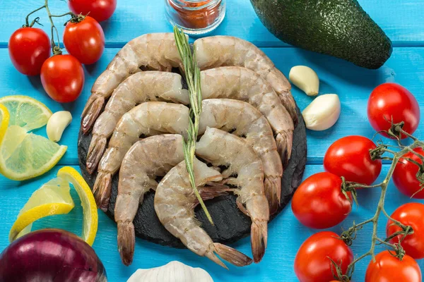 Beyaz karides, Pasifik beyaz karidesi ya da siyah tahta üzerinde limon, biberiye, domates, mavi ahşap arka planda avokado, üst manzara. seçici odak