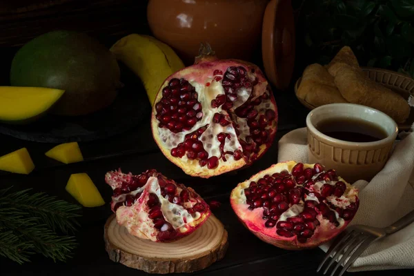 Siyah arka planda taze tropikal meyveler. Nar, muz, mango. Çay ve ballı meyveler. Sıcak bir aile akşamı konsepti. Rahatlık ve sıcaklık. seçici odak