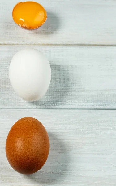 Taze tavuk yumurtası. İki tam tavuk yumurtası ve beyaz ahşap arka planda bir çatlak. Yumurta sarısı ve iki yumurta dikey olarak, boşluğu kopyala, seçici odak