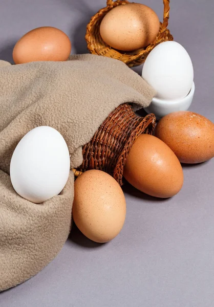 Hasır sepetteki tavuk yumurtaları gri arka planda. Dikey. Seçici odak, yakın plan