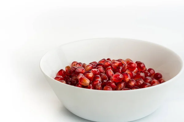 Beyaz arka planda, beyaz bir tabakta kırmızı nar tohumları. Beyaza izole edilmiş taze sulu nar tohumları. Yakın plan, kenar görünüm, seçici odak, kopyalama alanı