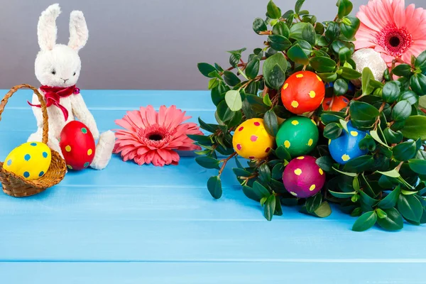 Paskalya tavşanı mavi ahşap bir arka planda oturur. Tavşan elinde bir yumurta ve paskalya yumurtasıyla hasır bir sepet tutuyor. Paskalya yumurtalı yeşil çimen. Mutlu Paskalya tebrik kartları. Boşluğu kopyala