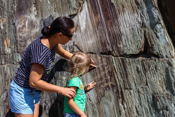 attractive woman shows daughters on petroglyphs rock paintings, Gorny Altai. natural icon and focal point of Altai indigenous people. monument conservation concept